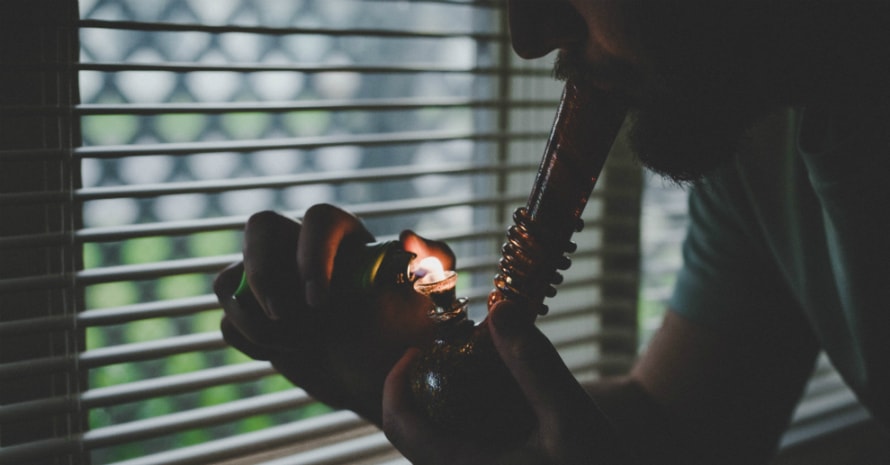 guy smokes a bong near the window